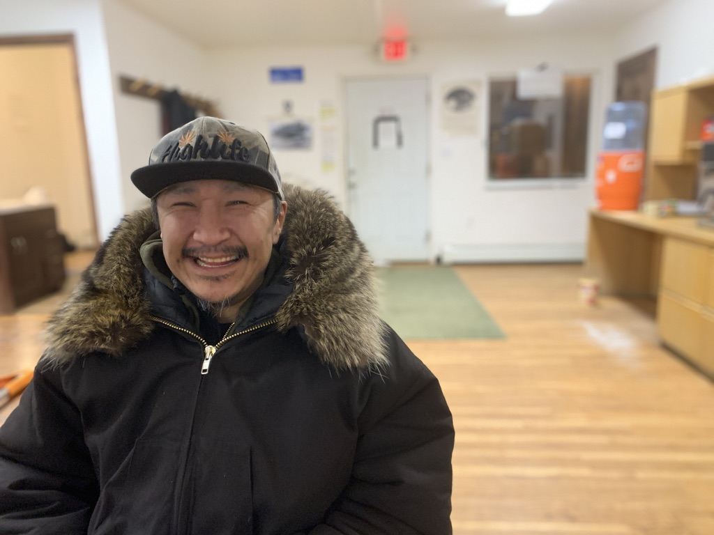 a man smiles inside, wearing a winter jacket